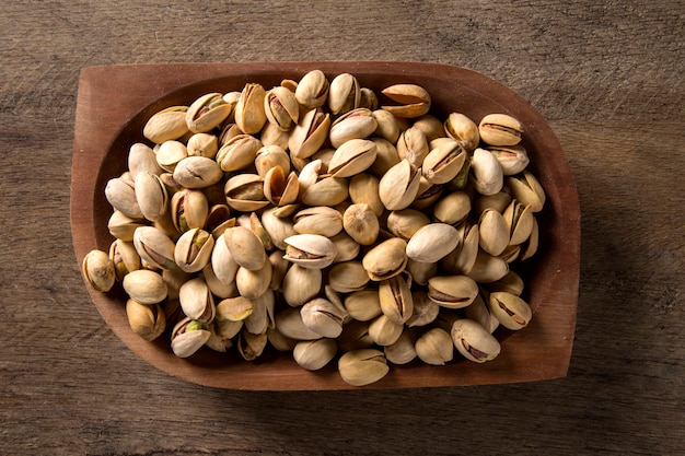 pistachio nuts in wood bowl with wood background.