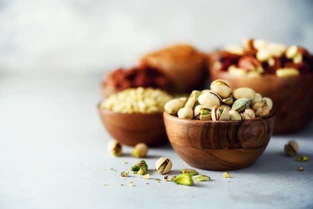 Pistachios nuts in wooden bowl. Assortment of nuts - cashew, hazelnuts, almonds, walnuts, pistachio, pecans, pine nuts, peanut, raisins