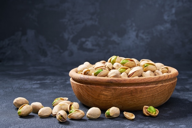 Pistachios in wooden bowl on black , close-up.