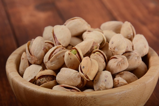 Pistachios in a wooden bowl on wooden surface pile of pistachios roasted pistachios in a bowl