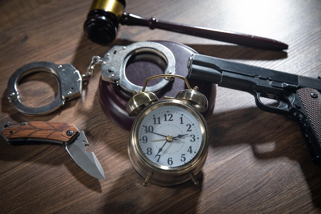 Pistol knife handcuffs judge gavel alarm clock on the wooden table