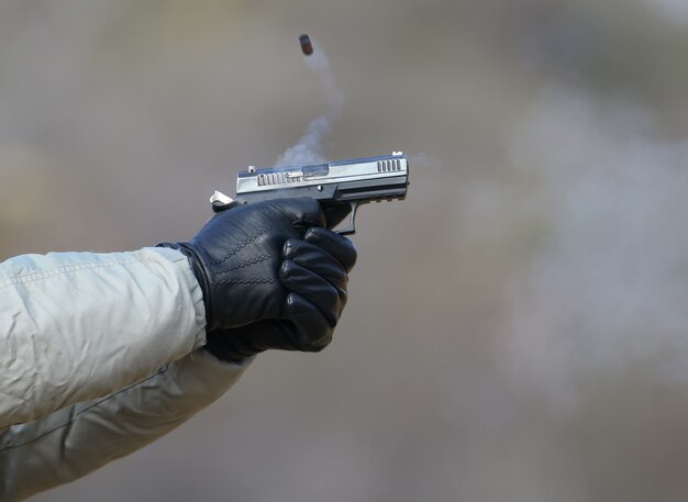 Tiro con la pistola a due mani, i proiettili che emanano dall'otturatore e il fumo blu.