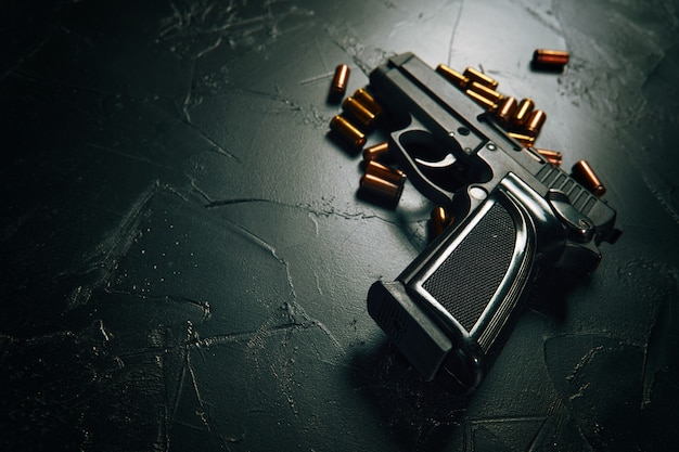 コンクリートのテーブルに弾丸が付いたピストル黒い銃と真ちゅう製のカートリッジ銃器クローズアップ武器の犯罪...