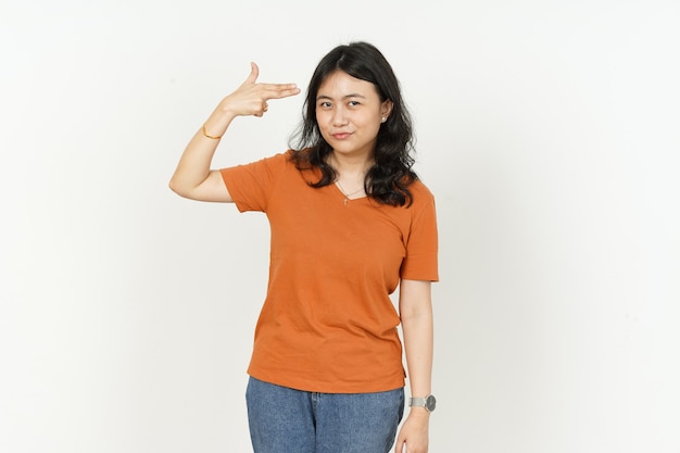 Pistoolvinger op hoofd van mooie aziatische vrouw die oranje t-shirt draagt dat op witte achtergrond wordt geïsoleerd