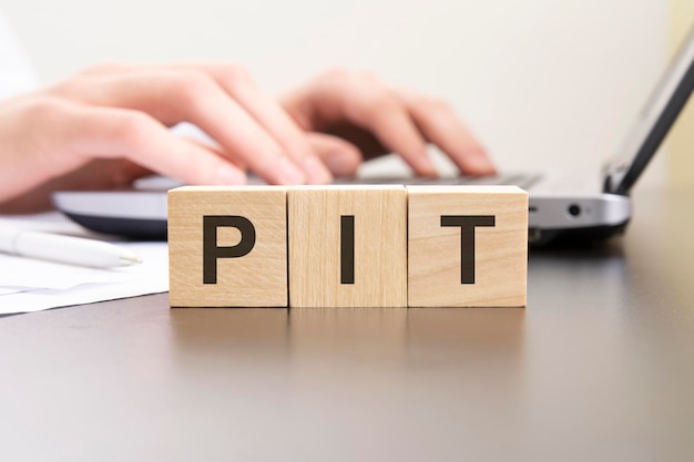 Pit acronym from wooden blocks with letters background hands on a laptop with blur business concept