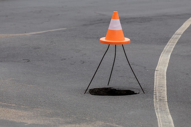 Pit hole on the road failure in the asphalt marked with an\
orange cone dangerous for travel earthquake the need for highway\
repair spaceship concept