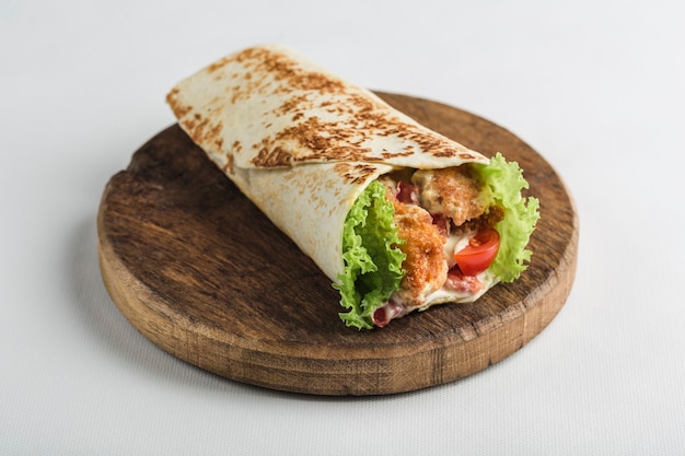 Pita bread roll with chicken and fresh vegetables on a wooden board on white