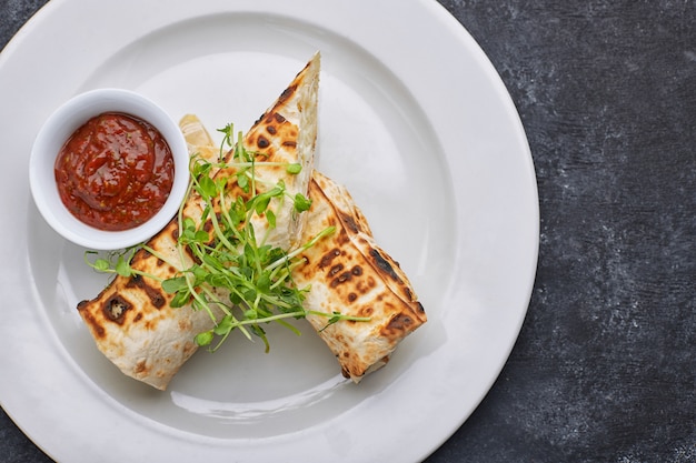 Pane pita con formaggio suluguni, salsa, microgreen, su un piatto bianco, su cemento scuro.