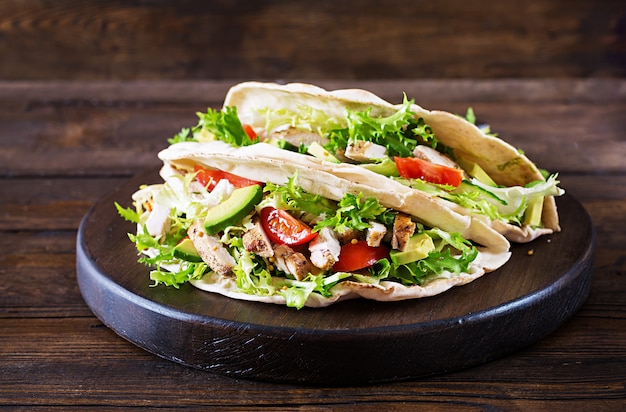 Pita broodsandwiches met gegrild kippenvlees, avocado, tomaat, komkommer en sla geserveerd op hout