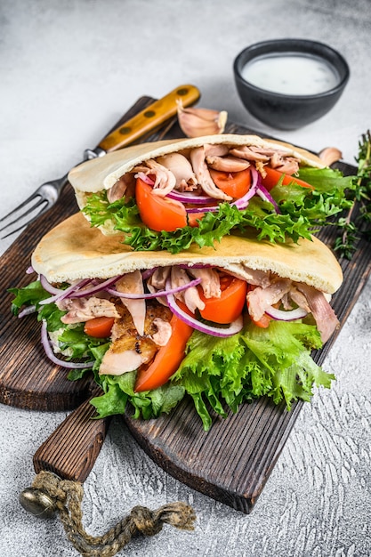 Pita sandwich with roasted chicken, vegetables and delicious sauce on white. Top view.