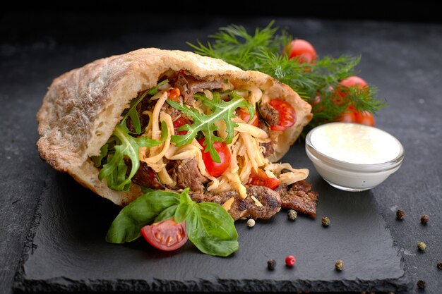 Pita with meat and vegetables, on slate, on a black table