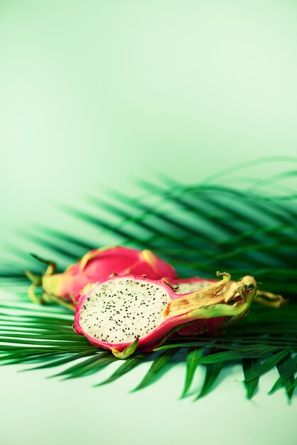 Pitahaya or dragon fruit over tropical green palm leaves on turquoise background. Pop art design, creative summer concept.