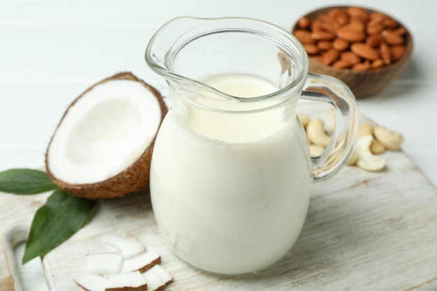 Pitcher of milk, coconut and nuts on white wooden table