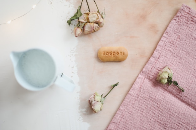 Brocca con rose di biscotti al latte e tovaglia di lino rosa su superficie rustica bianca