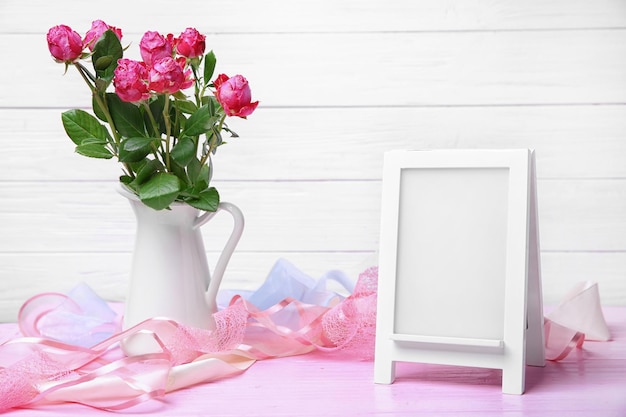 Pitcher with roses and empty frame on table