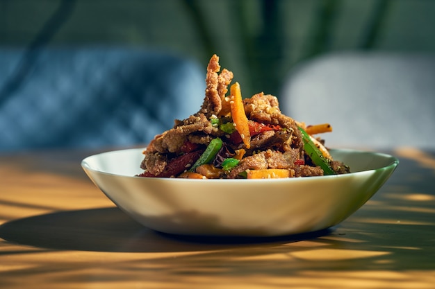 Pittig droog Sichuan wokrundvlees met peper, sesamzaad, wortel en groene tomaat in een witte kom. Chinese keuken