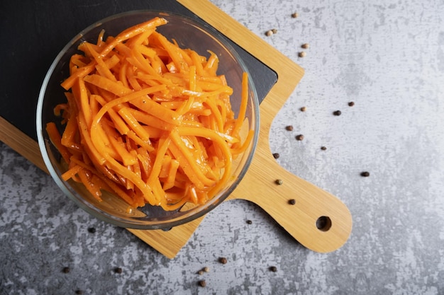 Pittige en pittige Koreaanse wortelsalade met saus en kruiden in een doorzichtige glazen slakom op een houten bord