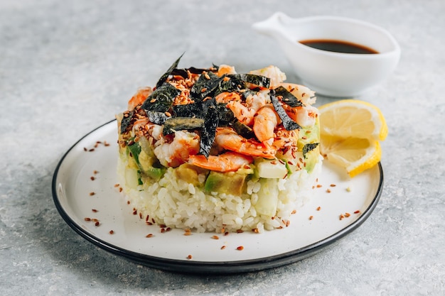 Pittige garnalensushi-stapels met lagen sushi-rijstkomkommers en avocado naast de pittige garnalen en furikake op lichte backgraund Selectieve focus