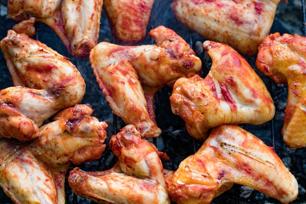 Pittige gemarineerde kippenvleugels grillen op een zomerbarbecue met hete vlammen in een close-up weergave.