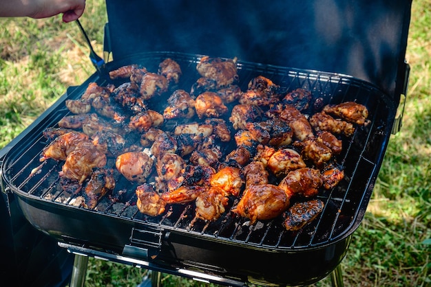 Pittige kippenpoten en -vleugels grillen op een rokend vuurtje in een draagbare barbecue