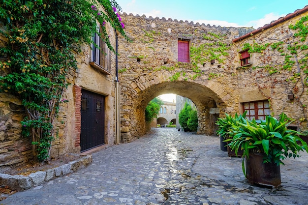 Pittoresk steegje met stenen bogen en de zon die bij zonsopgang tussen de huizen verschijnt Peratallada Girona Spanje