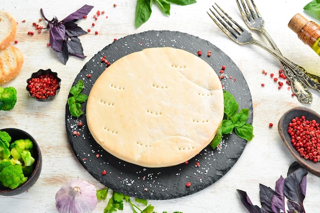 Pizza base on a black stone plate with basil Top view Rustic style