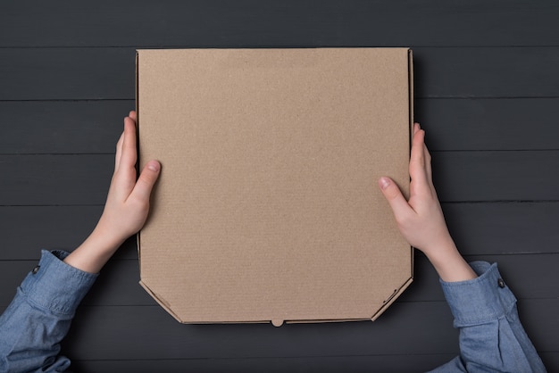 Pizza box in children's hands. Black background. Top view. Copy space.