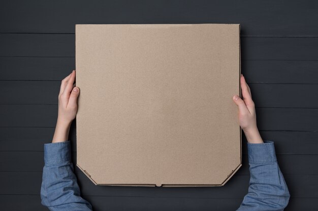 Pizza box in children's hands. Black wall. Top view. Copy space.