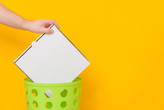 Pizza cardboard box is thrown into a green trash bin for recycling and recycling