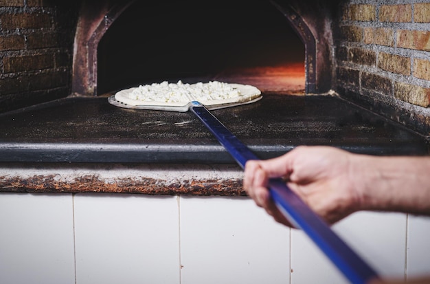 피자 요리사는 삽을 들고 손에 피자 세부 사항의 돌 오븐에서 흰색 피자 전용 모짜렐라를 굽습니다