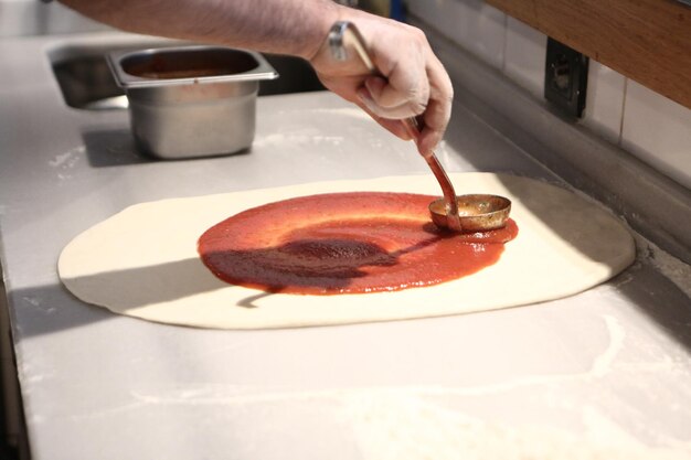 Pizza chef put sauce on base in a commercial kitchen