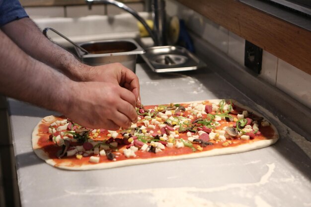 Il pizzaiolo ha messo la salsa sulla base in una cucina commerciale