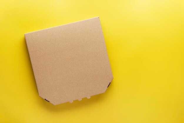 Pizza closed carton box on uniform yellow background flat lay mockup with blank space