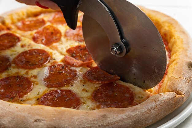 A pizza cutter is cutting a pepperoni pizza.