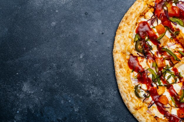 Pizza on a dark background. Classic italian pizza with tomatoes, pepper, vegetables, sauce and mazarella cheese on a dark kitchen table. Copy space