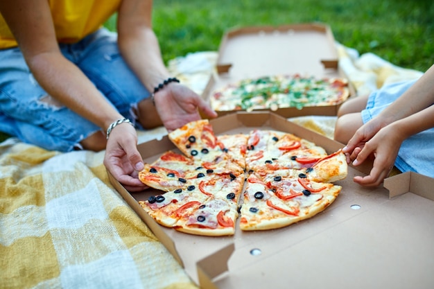 Pizza delen, handen een stuk pizza uit een doos buiten nemen, familiepicknick, pizza's eten voor het avondeten, fastfood bezorgen.