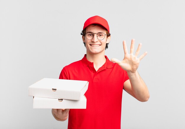 Pizza deliver boy smiling and looking friendly, showing number five or fifth with hand forward, counting down