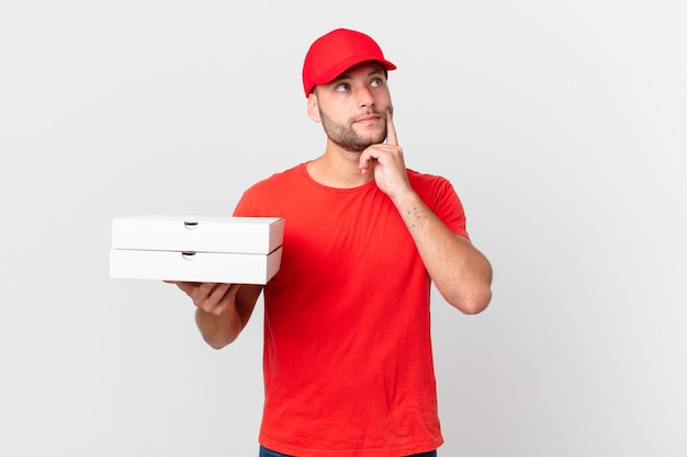 Pizza deliver man smiling happily and daydreaming or doubting