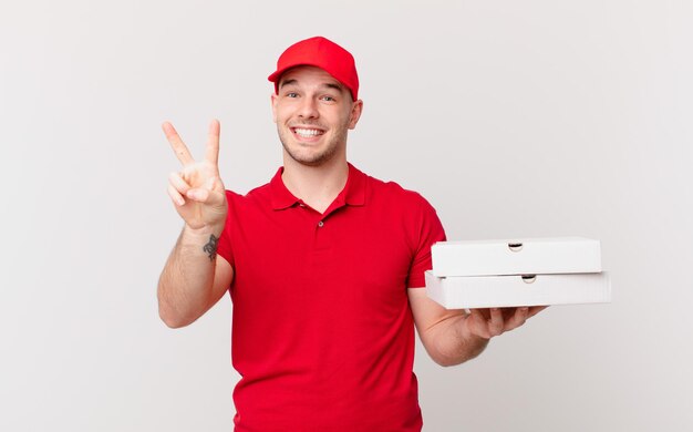 ピザは、笑顔で幸せそうに見え、のんきで前向きで、片手で勝利または平和を身振りで示す男を届けます