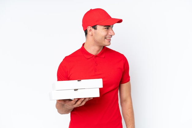 Pizza delivery caucasian man with work uniform picking up pizza boxes isolated on white background looking to the side and smiling