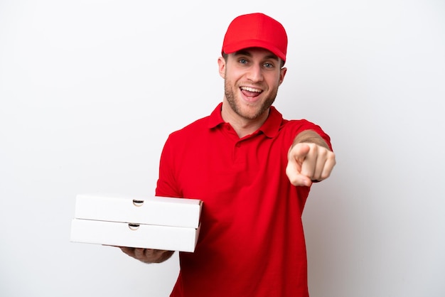 작업복을 입은 백인 피자 배달 남자가 흰색 배경에 격리된 피자 상자를 들고 놀라 앞을 가리키고 있다