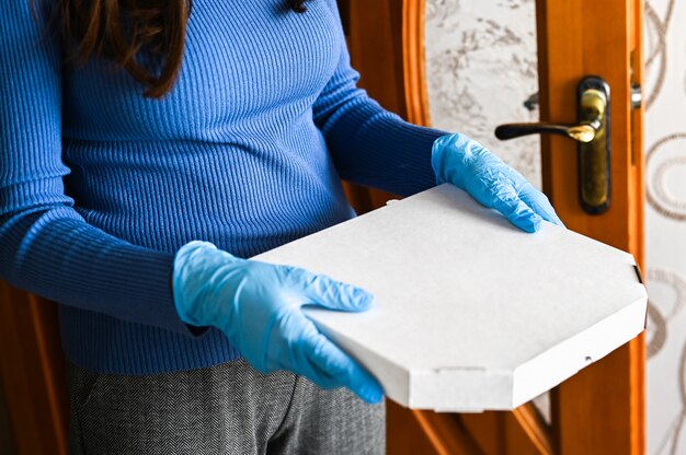 Pizza delivery in an epidemic. The girl neatly carries a box of pizza in gloves. Close-up. Food and Coronavirus