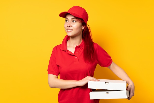 Pizza delivery girl holding a pizza over isolated wall looking to the side