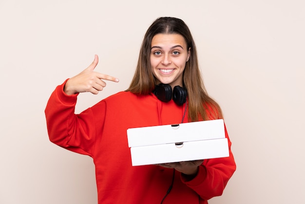 Pizza delivery girl holding a pizza over isolated wall and pointing it