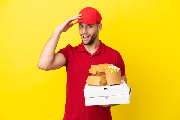 横を見ながら驚きのジェスチャーをしている孤立した背景の上にピザの箱やハンバーガーを拾うピザ配達人