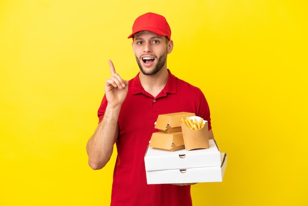 Pizza delivery man picking up pizza boxes and burgers over isolated background intending to realizes the solution while lifting a finger up