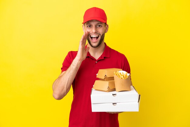 Доставщик пиццы собирает коробки для пиццы и гамбургеры на изолированном фоне с удивлением и шокированным выражением лица