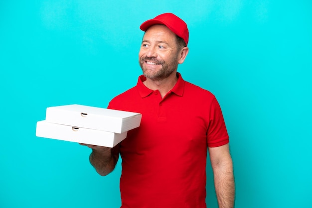 작업복을 입은 피자 배달원은 파란색 배경에 격리된 피자 상자를 들고 올려다 보면서 아이디어를 생각합니다