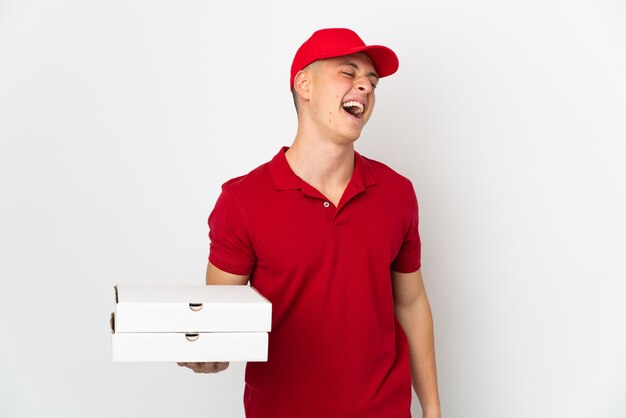 Pizza delivery man with work uniform picking up pizza boxes isolated on white wall laughing