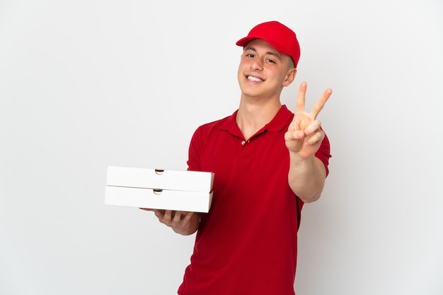 Pizza delivery man with work uniform picking up pizza boxes isolated on white wall smiling and showing victory sign